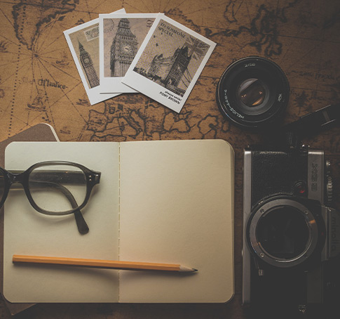 photo d'un carnet de la marque reverse ouvert sur la carte 'une mapemonde et entouré d'un appareil photo, d'un objectif et de photos